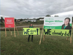Green candidate Megan Mitton holds us a sign saying "We already did!" beside a Liberal campaign sign which reads: "Save our hosptial, Vote Liberal."