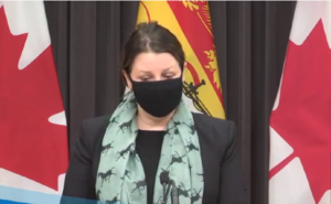 Dr. Jennifer Russell wears a mask and stands behind a podium.