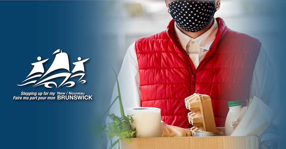 A person wears a mask and holds a box of groceries.