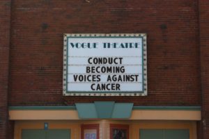 The Vogue Cinema marquee reads "Donduct Becoming Voice Against Cancer."