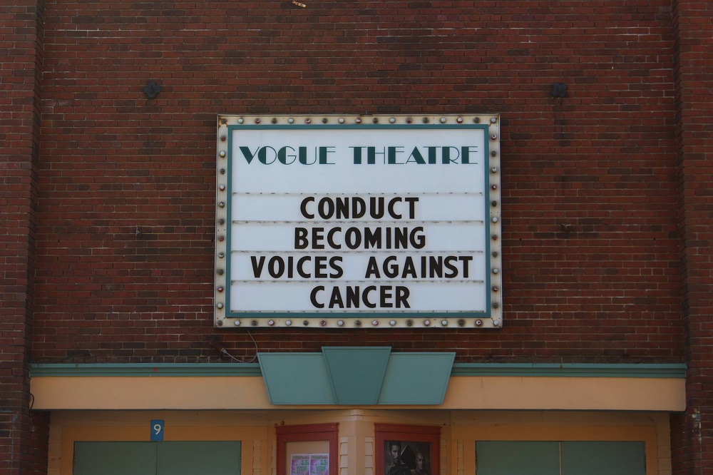 The Vogue Cinema marquee reads "Donduct Becoming Voice Against Cancer."