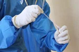 Person is blue gown and white gloves putting a swab in a container