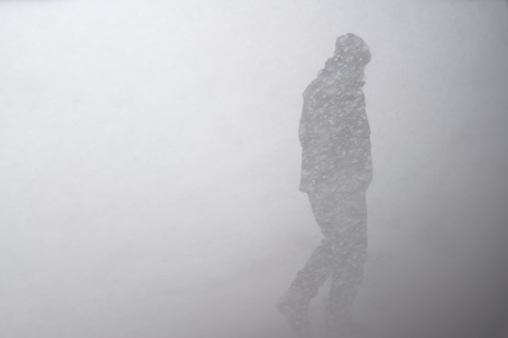 A silhouette of a person walks through a snowstorm.
