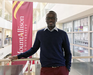 Ivan Okello smiles in front of a Mount Allison University banner.