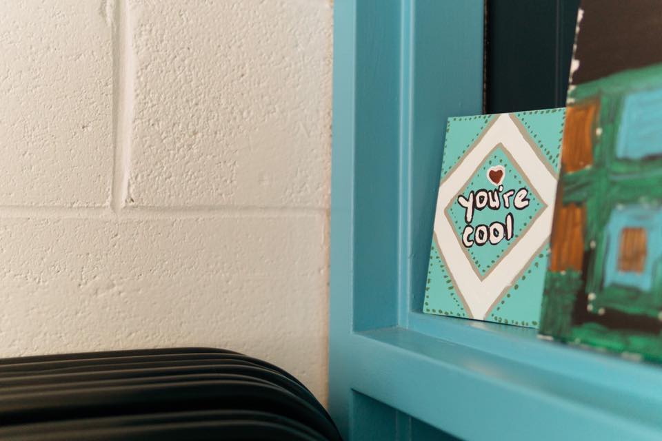 A small painting that reads "you're cool" sits on a blue shelf.