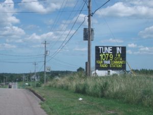 A road sign reads "Tune in 107.9 FM CFTA, You're true community radio station."