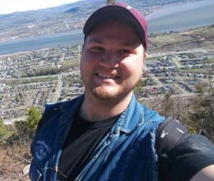 Man in baseball cap with scenery of a city behind him.