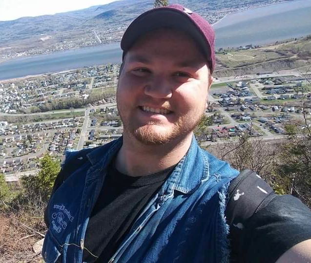 Man in baseball cap with scenery of a city behind him.