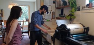 Amy Ward watches Keagan Hawthorne as he inspects a broadside he printed using his 1927 flatbed proofing press.