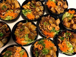 Black bowls filled with shrimp and vegetables are grouped together on a table.