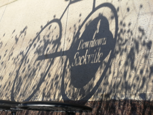 Shadow of a bike rack which says "Downtown Sackville" cast on a sidewalk.