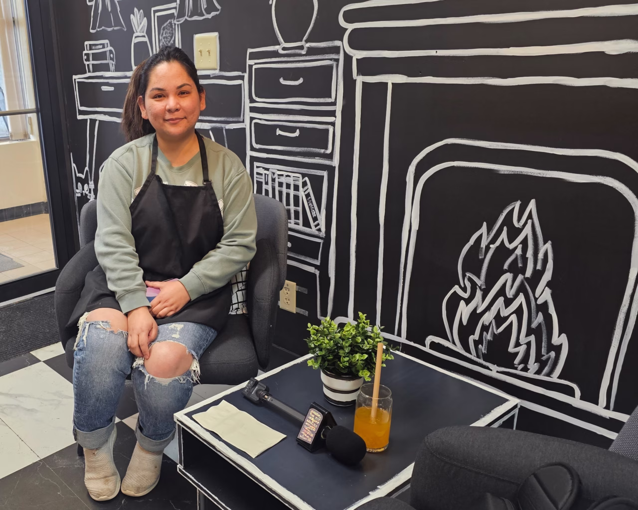 Business owner Mary Anne Catipon sits in front of her Cafe's wall art | Photo: Clinton Davis / CHMA News